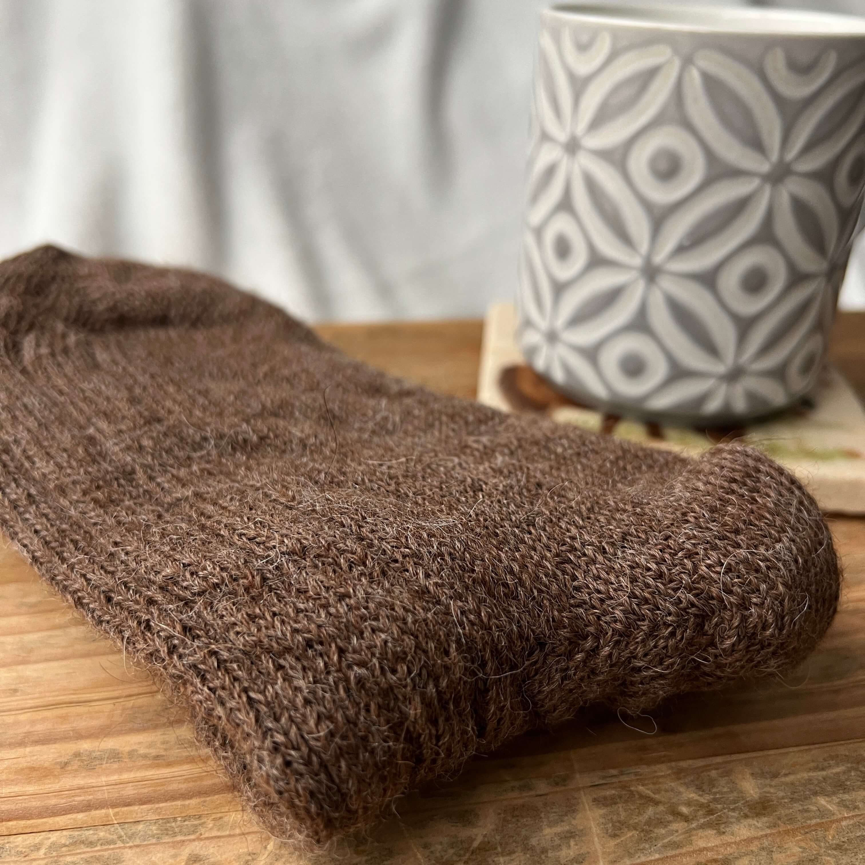 Brown alpaca bed socks folded alongside a hot beverage