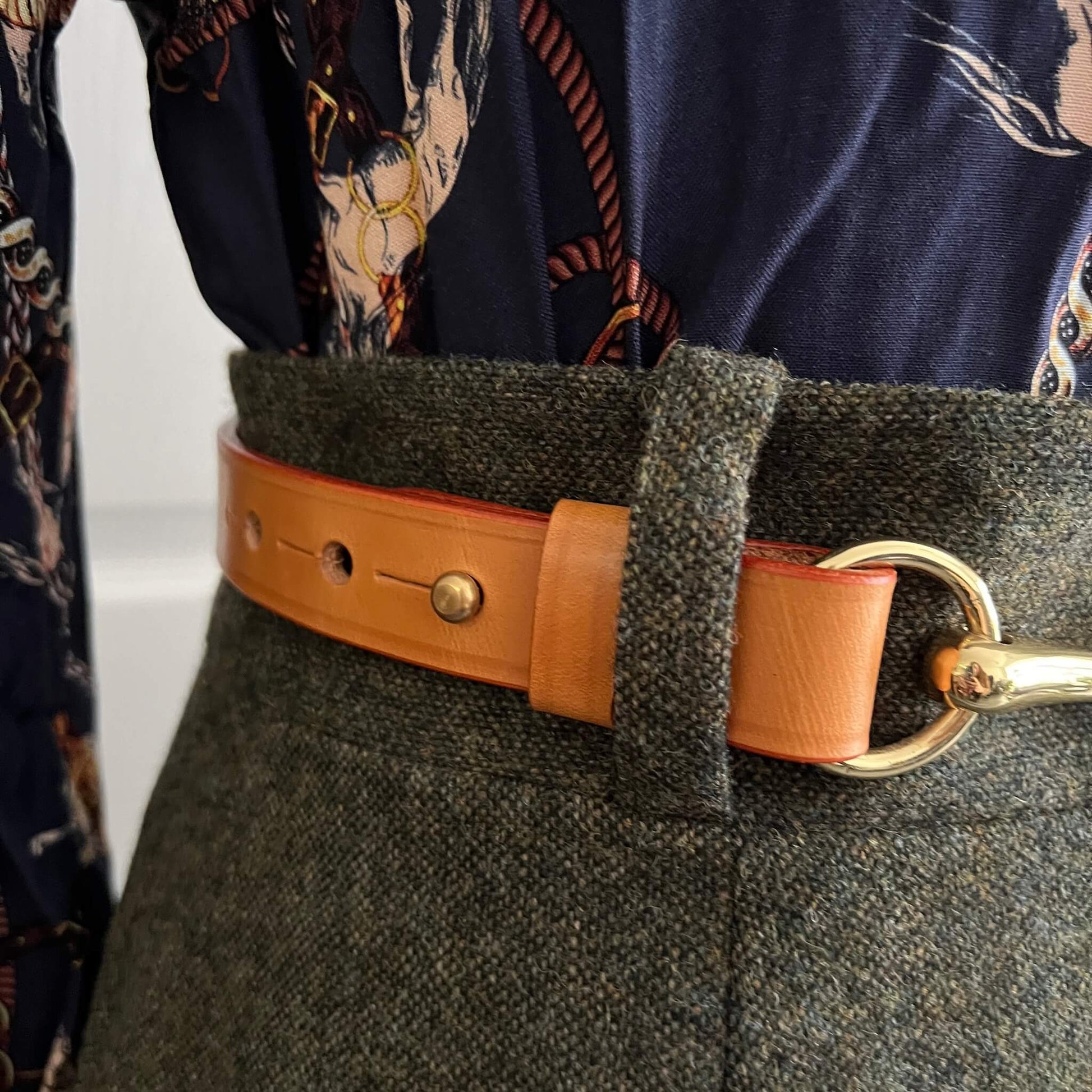 close-up of tan leather belt showing brass hardware