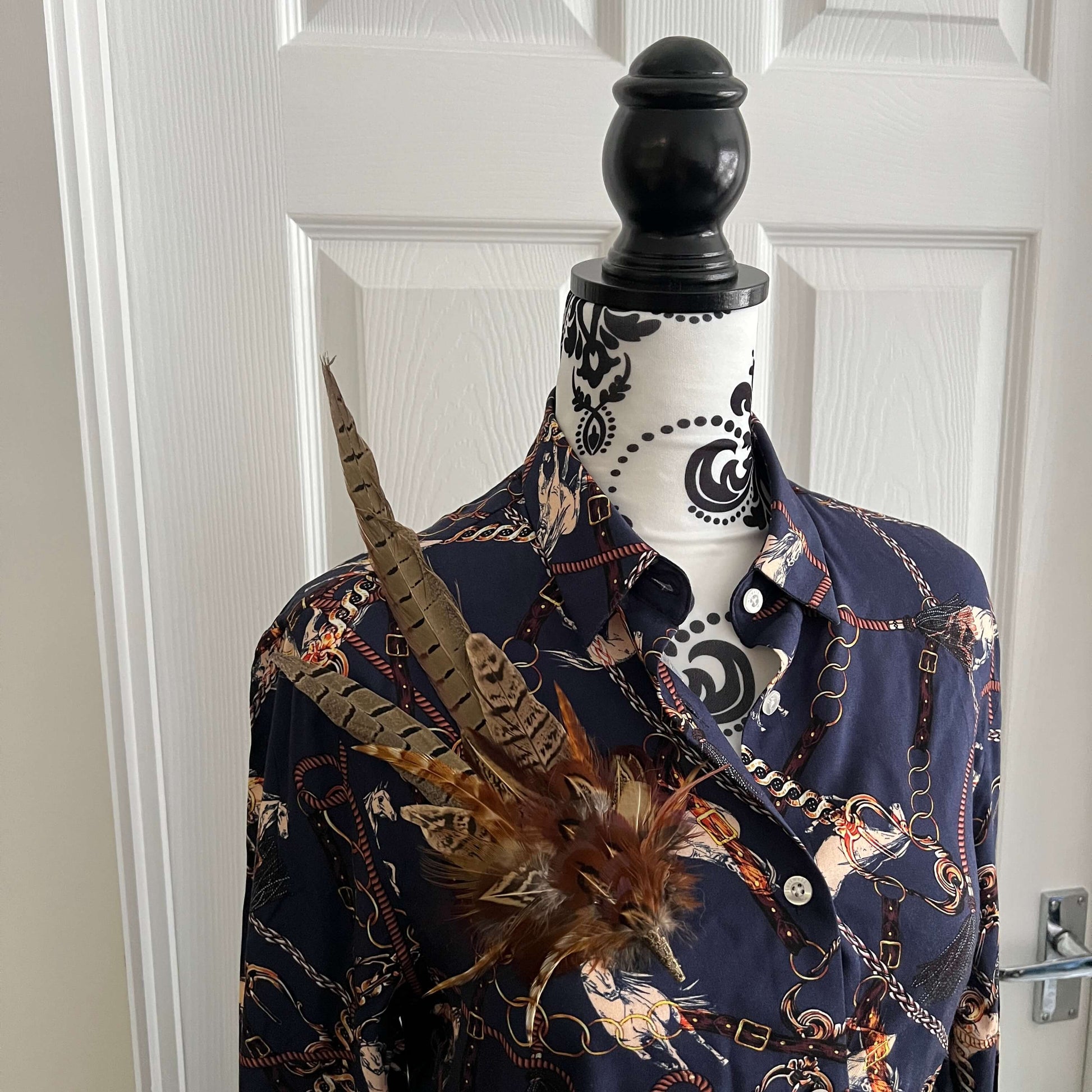 Mannequin wearing a large feather hat oin as a brooch with a blue equestrian shirt